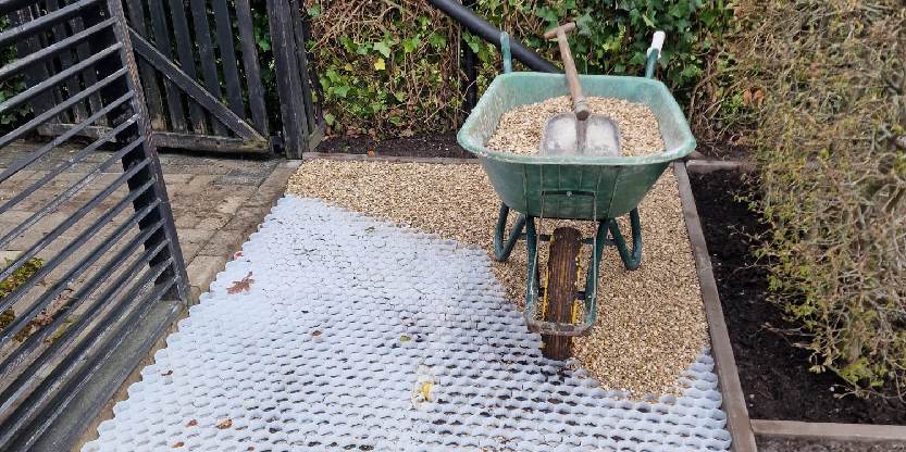 Een kruiwagen met grindplaten in een tuin waar ze grind aan het leggen zijn.